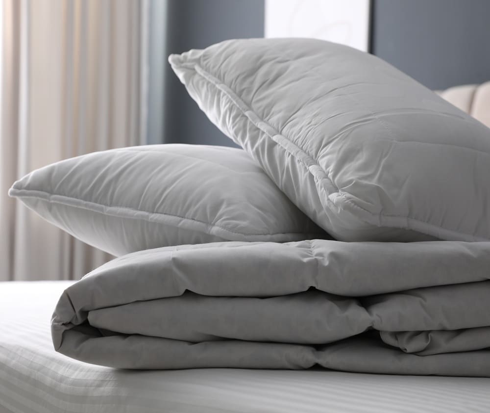 Two gray pillows stacked on top of a folded gray comforter, all placed on a white-striped bed.