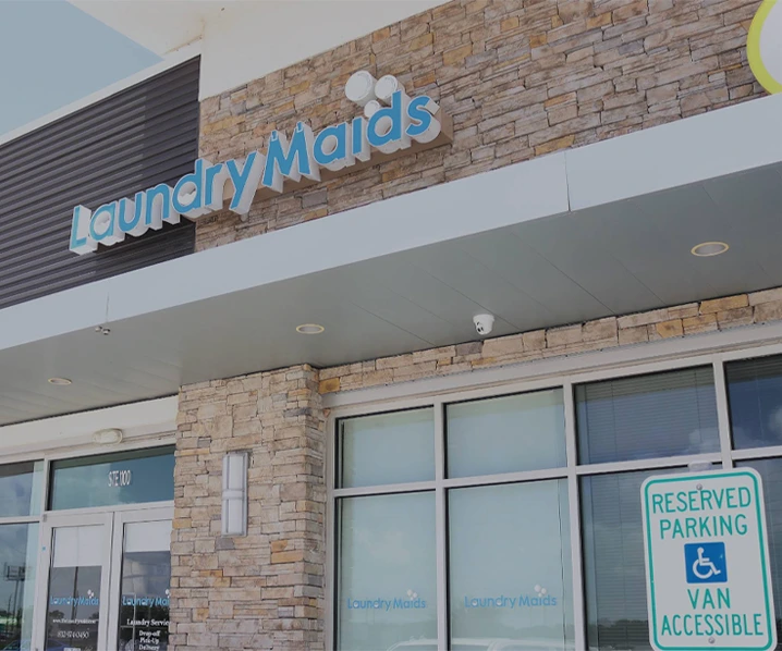 The exterior of a Laundry Maids store with a reserved handicap parking sign in front, featuring stone walls and large windows.