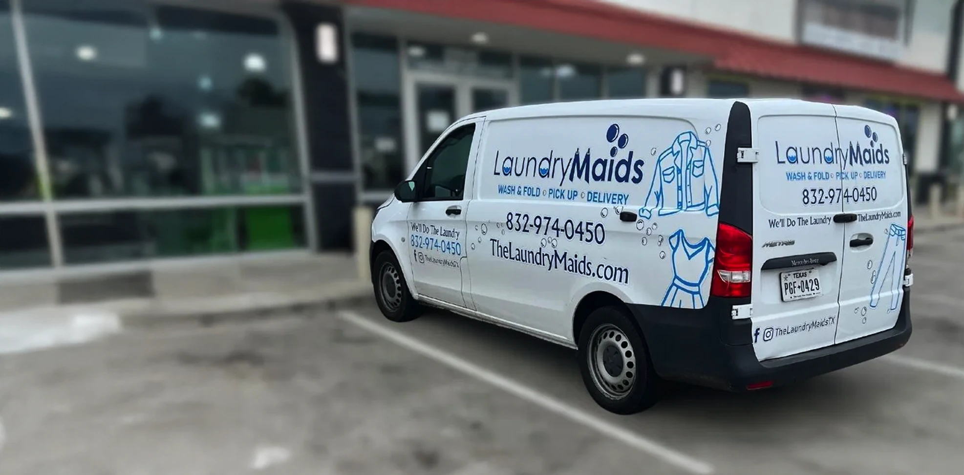 White van with "Laundry Maids" branding and contact information parked in front of a storefront in a parking lot.